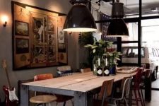 an industrial dining space with a sturdy wood and metal table, mismatching vintage chairs, black pendant lamps and a large artwork