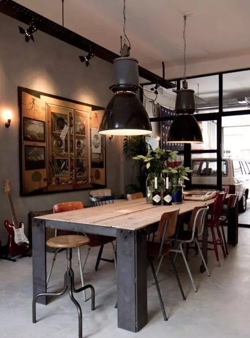 an industrial dining space with a sturdy wood and metal table, mismatching vintage chairs, black pendant lamps and a large artwork
