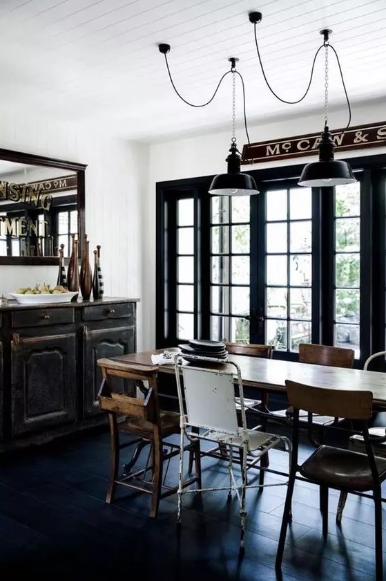 an industrial dining zone with a black vintage credenza, a stained table, mismatching chairs and black metal pendant lamps