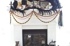 chic vintage Halloween mantel decor with feathers, blackbirds, buntings and garlands, witch hats and skulls is a bold and creative decor idea