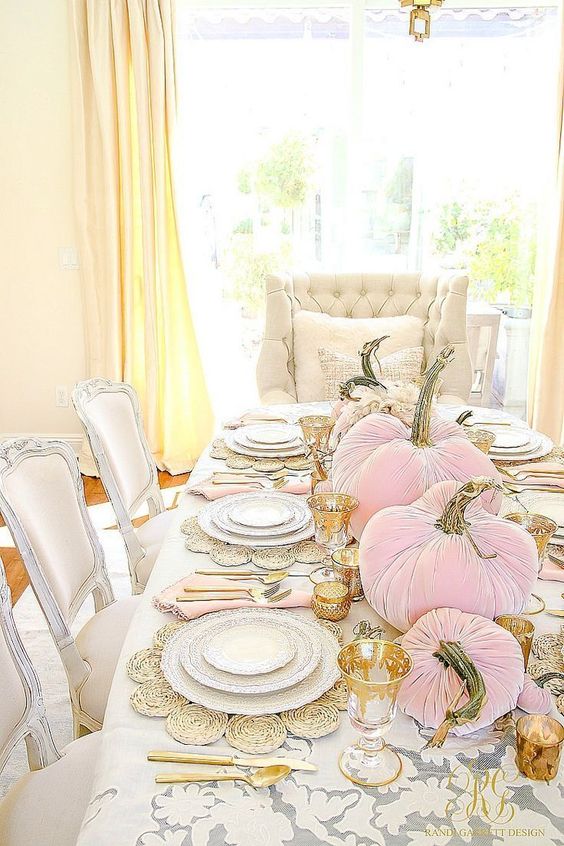 a chic glam Thanksgiving tablescape with woven placemats, gold rimmer glasses, pink velvet pumpkins and gold candleholders