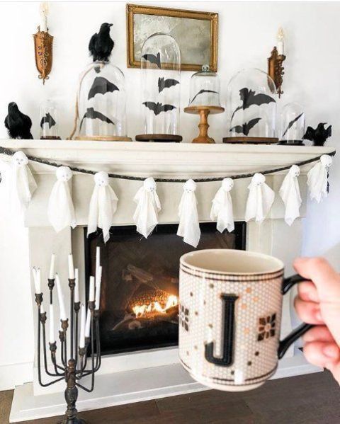 a Halloween mantel with black bats in cloches, blackbirds, a ghost garland of cheesecloth and a chic candelabra