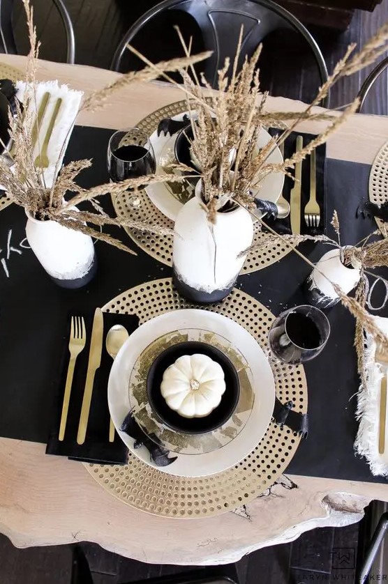 a chic black Thanksgiving tablescape with a dark runner, napkins, plywood placemats, wheat in a vase and gold cutlery
