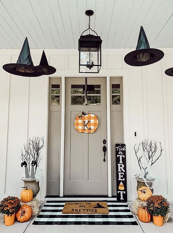 a stylish Halloween front porch with witch legs, witch hats, orange pumpkins and blooms