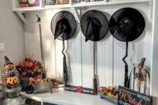 09 a traditional Halloween mudroom with black witches’ hats, brooms, pumpkins and faux pumpkins and a sign