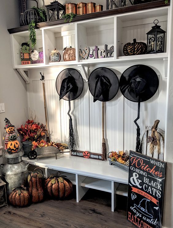 a traditional Halloween mudroom with black witches' hats, brooms, pumpkins and faux pumpkins and a sign