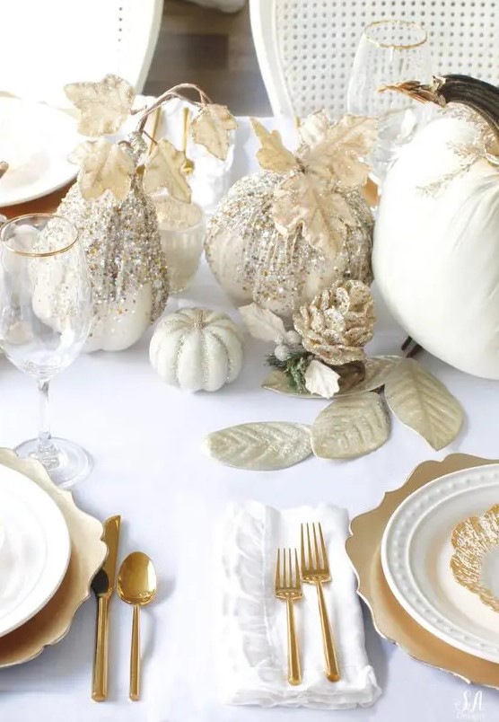 a glitz and glam neutral Thanksgiving tablescape with white linens, gold chargers and cutlery, white pumpkins decorated with glitter and gold leaves