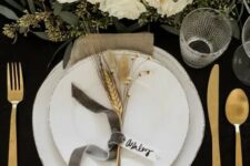 11 a gorgeous glam Thanksgiving table setting with a black uncovered table, white plates, gold cutlery, white florals and greenery and wheat