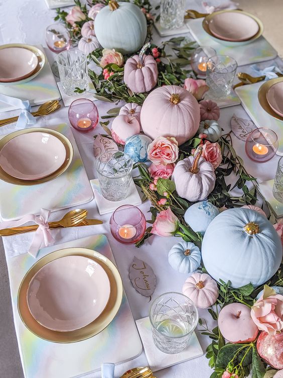 a pastel glam Thanksgiving tablescape with a greenery and pink bloom runner, pink and blue pumpkins, pink candleholders and pink plates