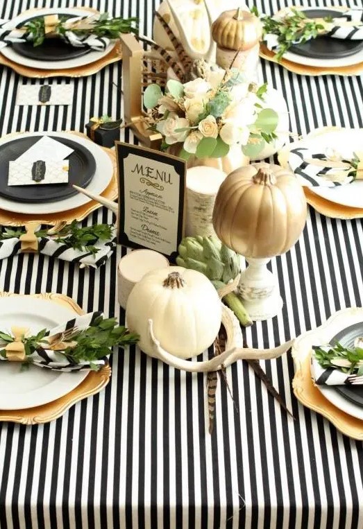 a modern glam tablescape with a black and white striped tablecloth, antlers, aux pumpkins, florals and gold chargers