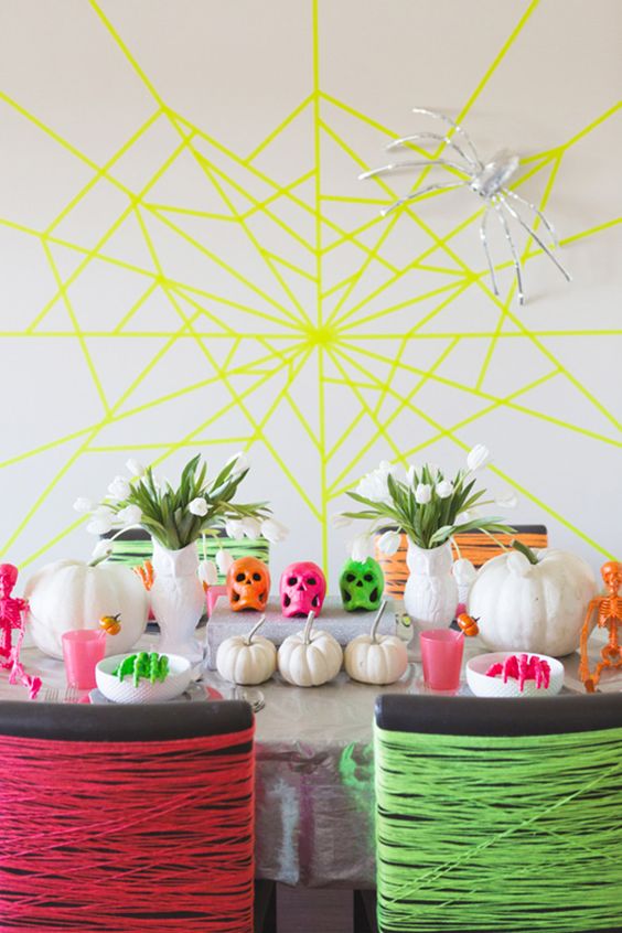 a bright neon Halloween party space with a yellow spiderweb, bold yarn covering the chairs and bright table decor