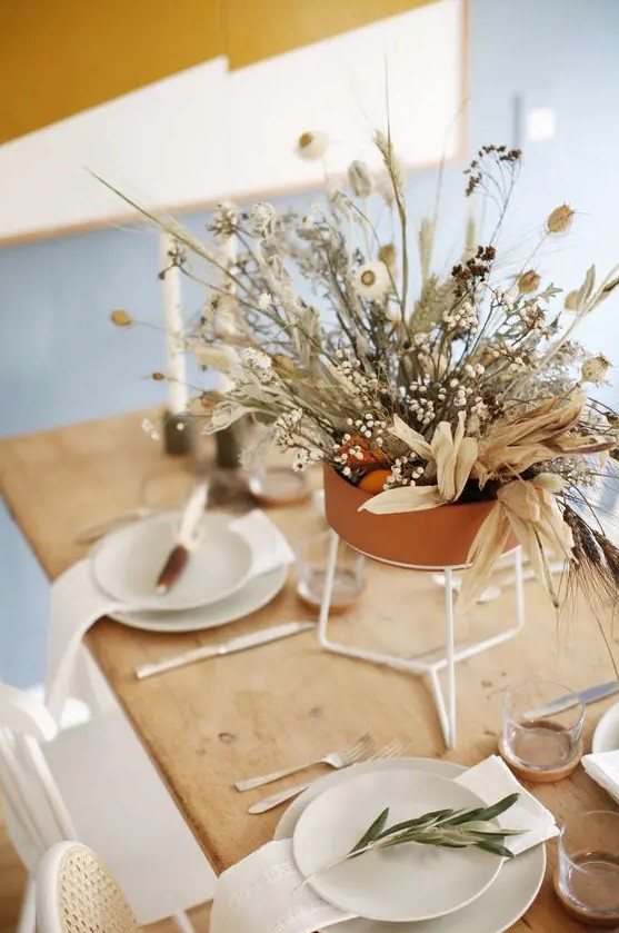 a modern organic Thanksgiving tablescape with white porcelain, greenery and a beautiful dried flower and herb centerpiece in a terracotta pot