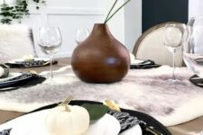 21 a modern Thanksgiving tablescape with a faux fur runner, black woven placemats, white porcelain and pumpkins, a brown vase with greenery