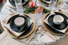 24 a simple modern Thanksgiving tablescape with gold chargers, black plates, white candles, evergreens, pomegranates and gold cutlery