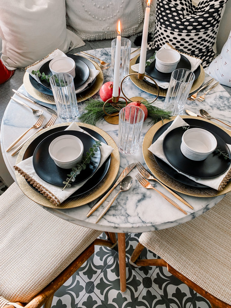 a simple modern Thanksgiving tablescape with gold chargers, black plates, white candles, evergreens, pomegranates and gold cutlery