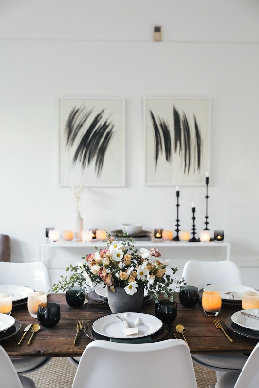 a stylish modern Thanksgiving tablescape with black and orange glasses, black chargers and white plates and neutral and pastel blooms is pure chic