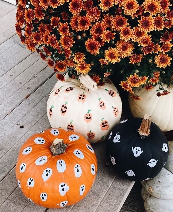 a white, orange and black pumpkin decorated with sharpie ghosts and jack-o-lanterns look very nice