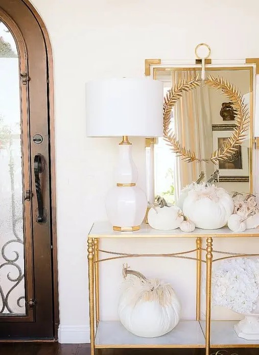 beautiful Thanksgiving console table styling with white fabric pumpkins topped with feathers, with fabric blooms and a gold leaf wreath