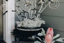 29 crazy Halloween front porch decor with a spellbook, a black planter with oversized blooms, a black cauldron with twigs and black bats