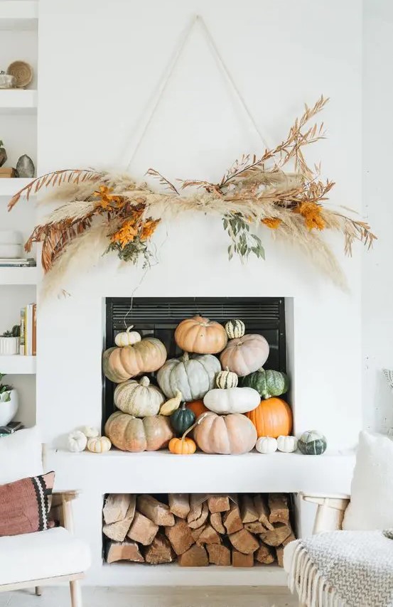 a modern fall or Thanksgiving fireplace filled with various natural pumpkins, with a pampas grass and greenery overhead decoration