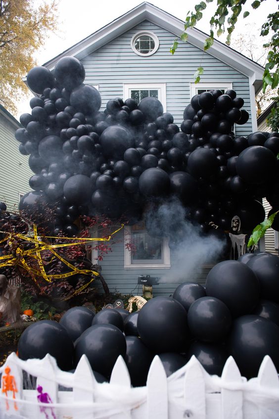 a Halloween backyard decorated with black balloons, with trees, blooms and gravestones is a lovely space