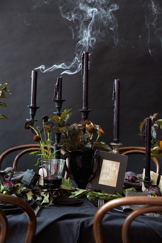 a black Halloween tablescape with black linens, black and purple candles, greenery and dark blooms is amazing