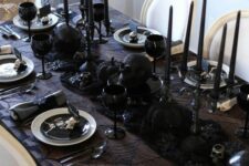 a black Halloween tablescape with black linens, black skulls, spiders, candles, plates and white napkins and chargers