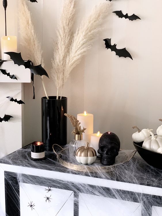 a black skull candle, a black vase and black bats on the wall, fireplace and mantel plus some neutrals candles and pumpkins