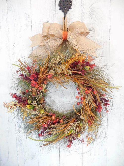 a bright rustic Thanksgiving wreath with grasses, twigs, fruits and berries and some bold blooms plus a burlap ribbon bow on top