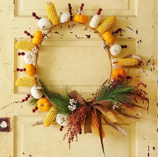 a bright rustic fall wreath made of yellow and white pumpkins and gourds, corn cobs, cranberries, greenery and berries plus a ribbon bow