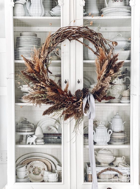a dried fall or Thanksgiving wreath of dried grasses, lotus slices, some branches and a grey ribbon bow is quite elegant