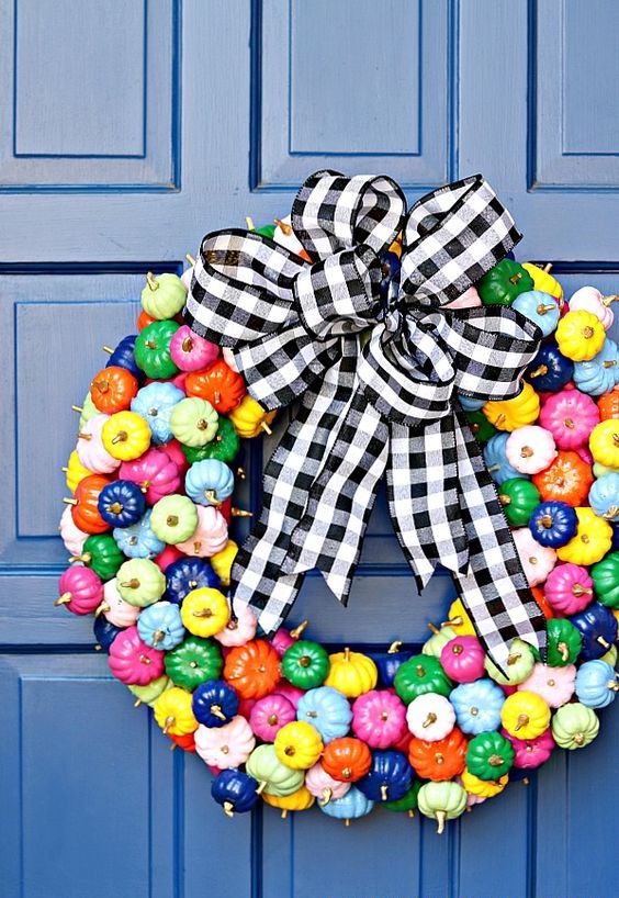 a super colorful mini pumpkin wreath with gilded stems and a black and white plaid bow on top is amazing for the fall
