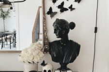 stylish Halloween decor with a black bust and black butterflies, a white skull and roses plus a candle in a black glass