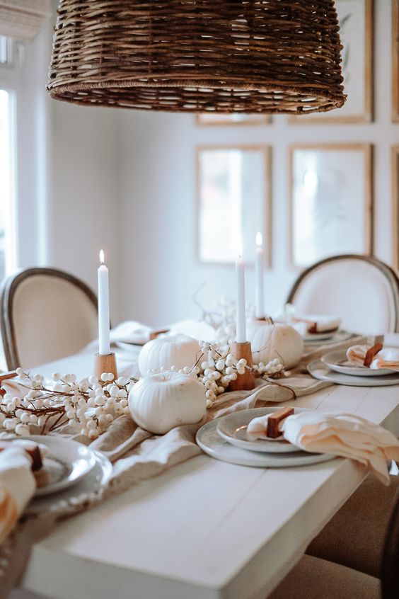 a beautiful Thanksgiving tablescape with white candles and pumpkins, grey plates and neutral linens, wooden candleholders and berries