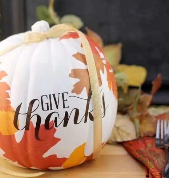 a beautiful white pumpkin with decoupaged fall leaves on it and a yellow ribbon is a chic decoration for Thanksgiving
