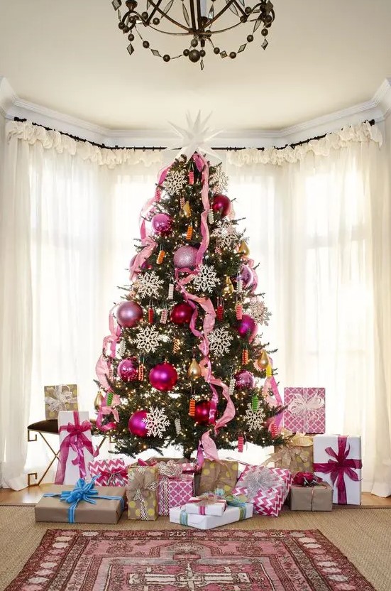 a bold Christmas tree decorated with pink and pink sequin ornaments, pink ribbons, lights and large snowflakes and a large star on top