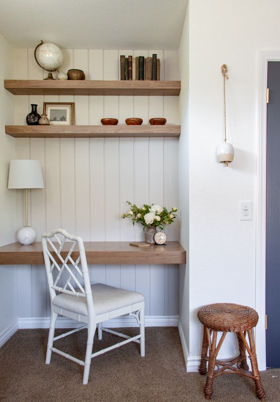 a farmhouse home office nook with built in shelves and a desk, a white chair, a woven stool and some decor and books