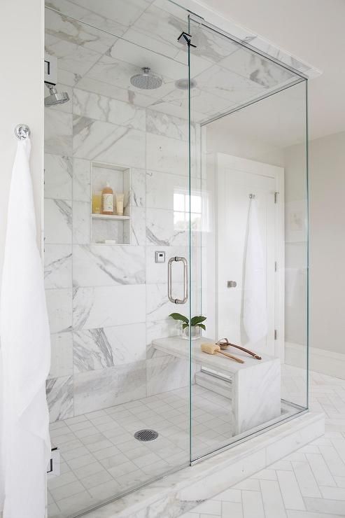 a contemporary white bathroom clad with marble and herringbone tiles, with a shower with glass doors and neutral fixtures