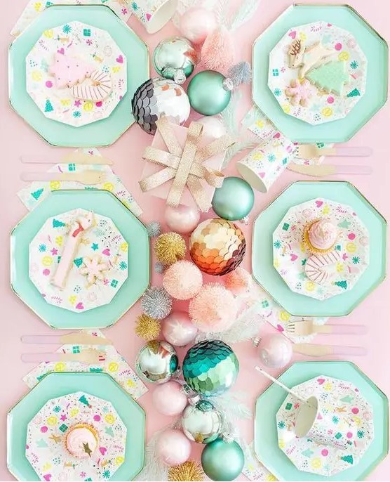 a lovely pastel Christmas tablescape with a pink tablecloth, mint grene hex plates, a pastel ornament garland and bright plates