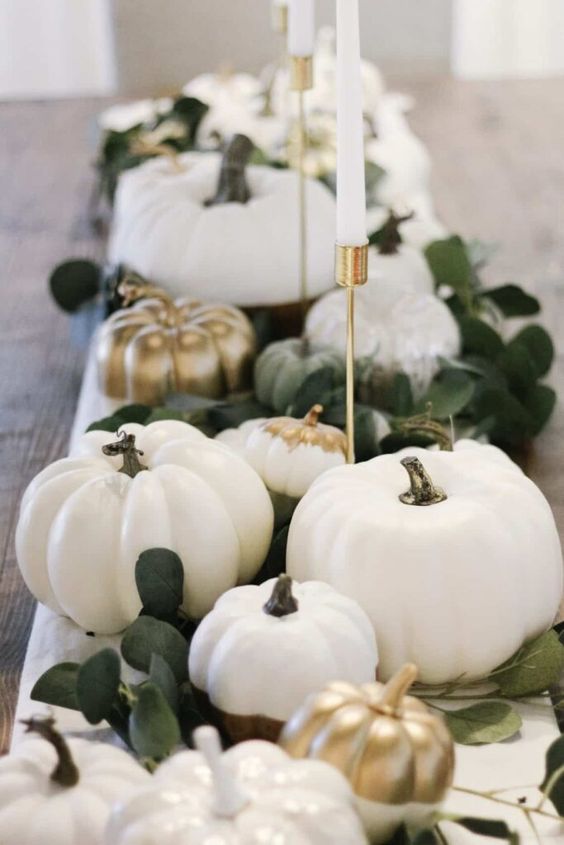 a Thanksgiving centerpiece of white and gilded pumpkins, leaves and candles in gold candelholders is a stylish idea
