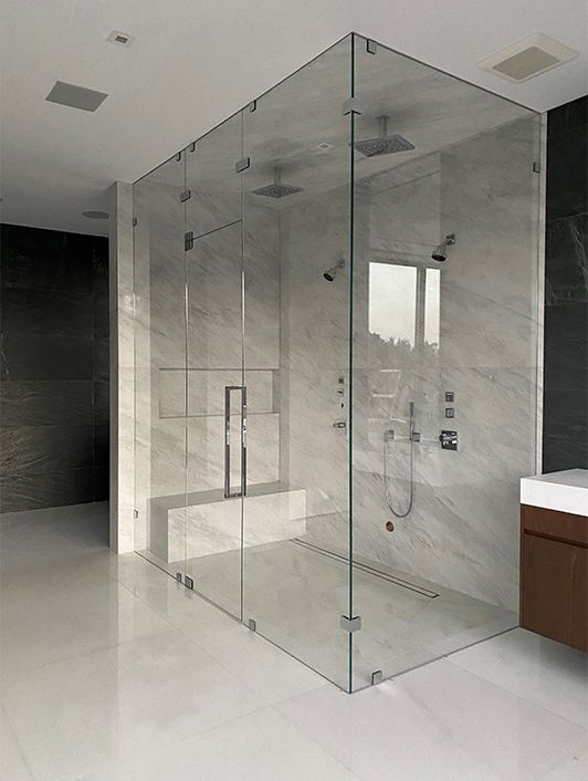 a minimalist bathroom with a shower space clad with marble and enclosed in glass, a marble slab bench for sitting there