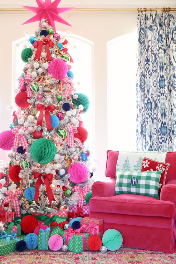 a flocked Christmas tree decorated with hot pink, red and green paper pompoms, smaller usual pompoms and ornaments