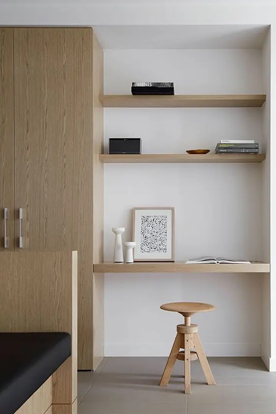 a minimalist awkward nook with built in shelves and a desk, with a wooden stool and books plus candle lanterns is amazing