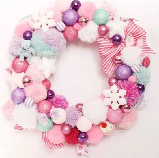 a pastel Christmas wreath of pompoms and ornaments, stars and snowflakes and striped ribbons is a pretty decoration