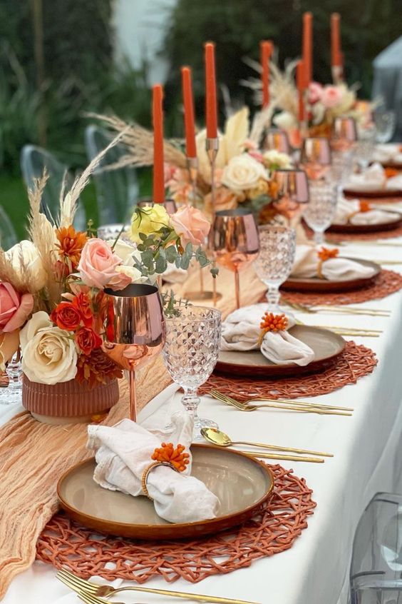 a colorful boho Thanksgiving tablescape with a yellow runner, bright blooms and grasses, orange woven placemats and copper glasses
