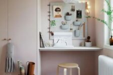 a small awkward nook by the window, with a built-in desk and a pegboard with various stuff, greenery and art