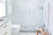 08 a small serene bathroom with white subway tiles, patterned ones on the floor, a shower space with clear glass doors and a handle