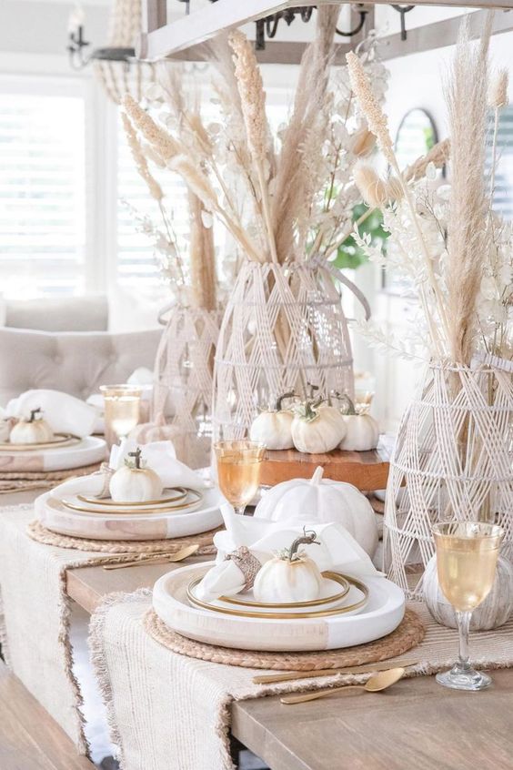 a cool rustic meets boho Thanksgiving tablescape with pampas grass in yarn covered vases, white faux pumpkins, large wooden chargers and woven placemats