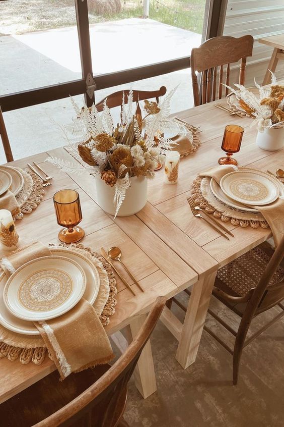 a cozy boho Thanksgiving tablescape with woven placemats, printed plates, warm colored napkins and lovely dried flower centerpieces