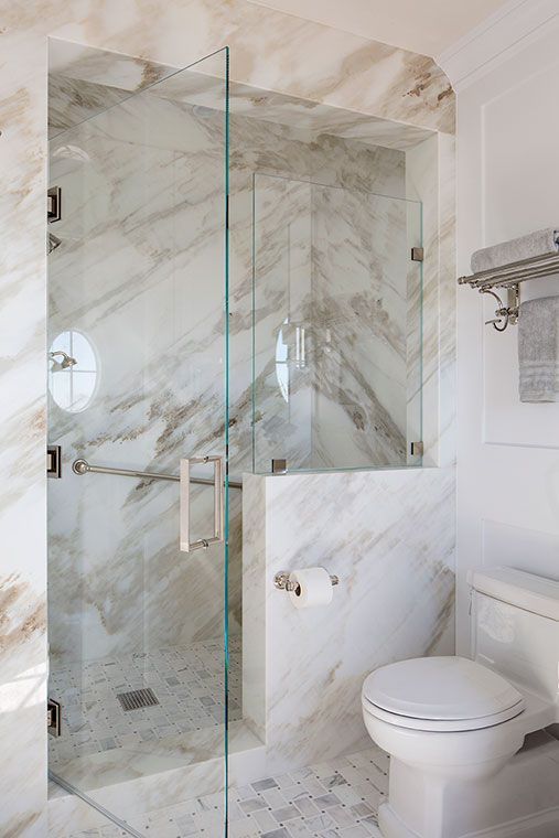 a small and chic bathroom clad with marble, with a shower space featuring a glass door and railing